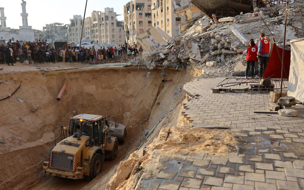 People and members of the International Committee of the Red Cross (ICRC) watch as Palestinians use an excavator to dig deep into the ground, reportedly searching for bodies of hostages, in Khan Younis in the southern Gaza Strip on October 17, 2025 (Omar AL-QATTAA / AFP)