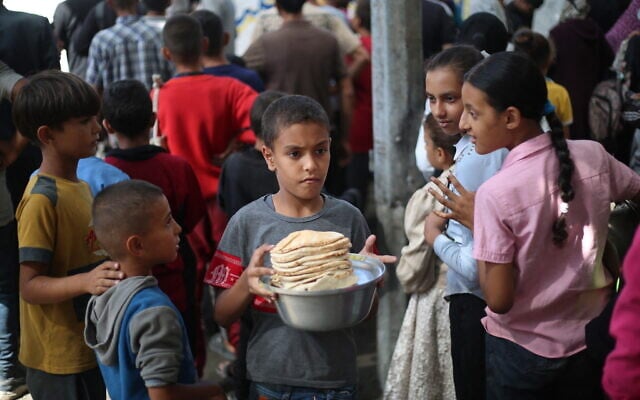 Palestinian children gather to receive food portions from a charity kitchen in the Nuseirat refugee camp, located in the central Gaza Strip, on October 21, 2025 (Eyad BABA / AFP)