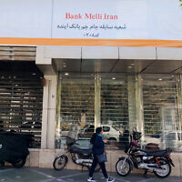An Iranian woman walks past a branch of the state-owned Melli Bank, which absorbed the assets of the now-defunct Ayandeh Bank, with signage on its facade reading in Farsi "This former Ayandeh Bank branch is now part of Melli Bank," in the capital Tehran on October 25, 2025. (ATTA KENARE / AFP)