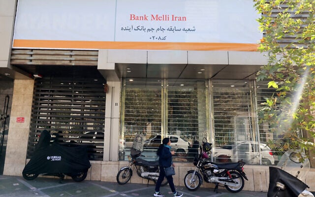 An Iranian woman walks past a branch of the state-owned Melli Bank, which absorbed the assets of the now-defunct Ayandeh Bank, with signage on its facade reading in Farsi "This former Ayandeh Bank branch is now part of Melli Bank," in the capital Tehran on October 25, 2025. (ATTA KENARE / AFP)