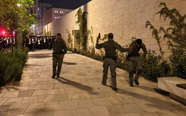 A police officer holds his pistol as he helps an injured comrade, as ultra-Orthodox men protest against mandatory military conscription, in Jerusalem on October 30, 2025. (Fadel Senna/AFP)