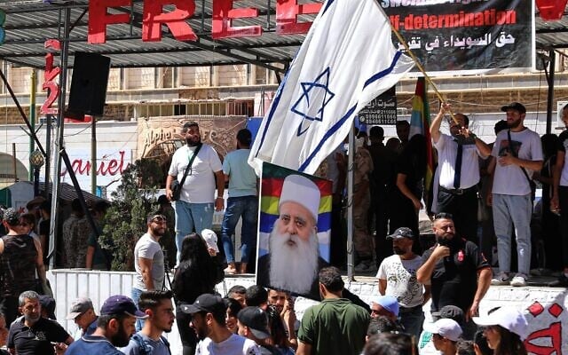 A man waves an Israeli flag over a picture of Sheikh Muafak Tarif, the spiritual leader of the Druze in Israel, during a weekly rally in Sweida, southern Syria, on September 20, 2025. (AP Photo/Fahd Kiwan)