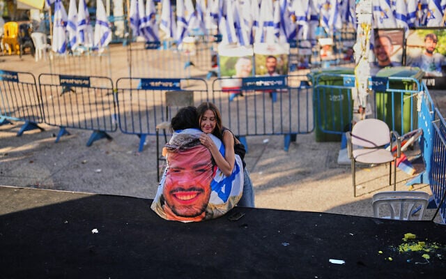 A woman, left, wrapped with an Israeli flag with the photo of one of her best friend Itay Chen, who was killed in Hamas' attack on October 7, is embraced at the plaza known as Hostages Square, in Tel Aviv, Israel, October 14, 2025. (AP Photo/Francisco Seco)