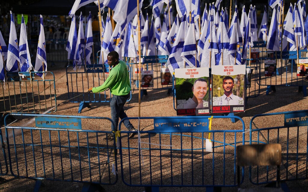 A worker cleans at Hostages Square, behind images of slain hostages Bipin Joshi and Yossi Sharabi, in Tel Aviv, Israel, Tuesday, Oct. 14, 2025. (AP Photo/Francisco Seco)