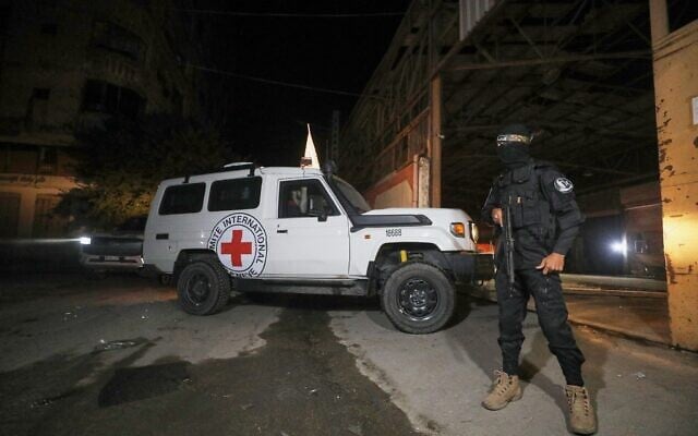 A gunman wearing the uniform of the al-Qassam Brigades, the military wing of Hamas, stands guard as Red Cross vehicles enter a warehouse to collect coffins said to contain the bodies of four hostages, in Gaza City, October 14, 2025. (AP Photo/ Yousef Al Zanoun)