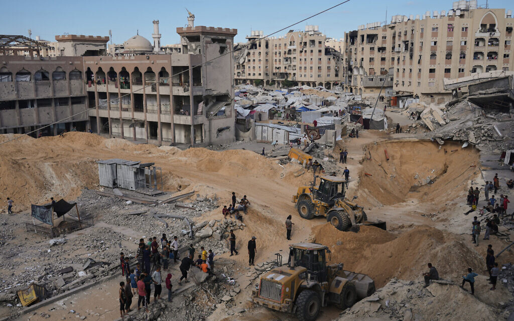 Palestinians watch Hamas members search for bodies of hostages in an area in Hamad City, Khan Younis, in the southern Gaza Strip, October 18, 2025. (AP Photo/Jehad Alshrafi)