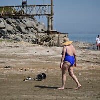 People walk along the Sea of Galilee shore, where water used to be, past infrastructure once submerged, at Kibbutz Ginosar, northern Israel, October 4, 2025. (Michael Giladi/Flash90)
