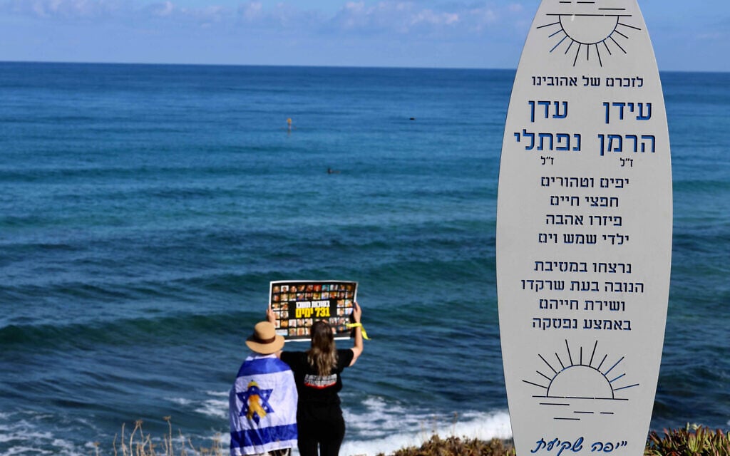 Surfers at Palmachim beach mark two years since the October 7, 2023 massacre, next to a memorial for Idan Herman and Eden Naftali, who were murdered at the Nova music festival, October 7, 2025. (Oren Cohen/Flash90)