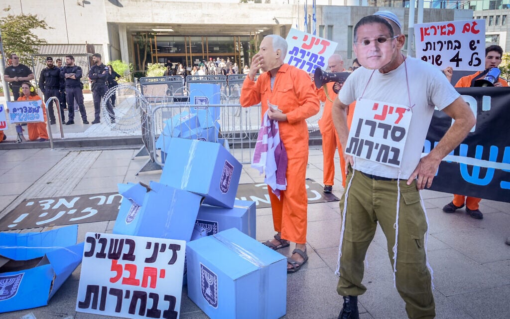 Activists display signs charging the new Shin Bet chief David Zini will "sabotage" democratic elections, in a protest against Prime Minister Benjamin Netanyahu outside the Tel Aviv District Court, where the premier is supposed to testify in his corruption trial, October 15, 2025. (Avshalom Sassoni/Flash90)