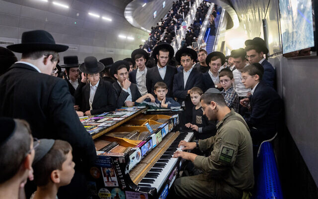 Ultra-Orthodox Jews gather around an Israeli soldier playing the piano at the Yitzhak Navon train station in Jerusalem, on their way to attend the "million man" protest against IDF conscription, in Jerusalem, October 30, 2025. (Chaim Goldberg/Flash90)