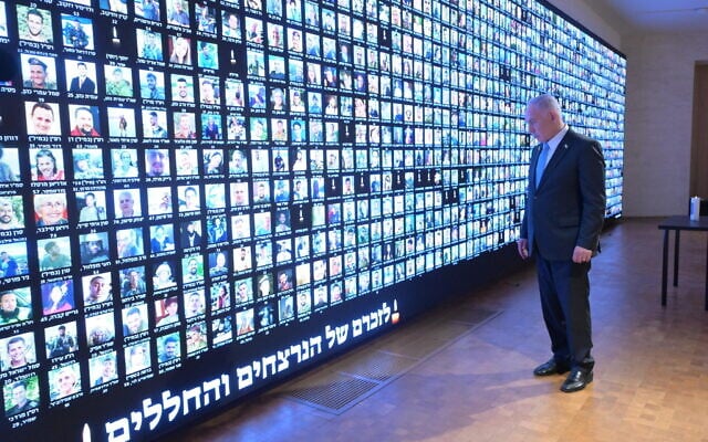 Prime Minister Benjamin Netanyahu pays respect to the victims of the war against Hamas in Gaza, next to a wall with faces of victims, at the National Library of Israel in Jerusalem, October 12, 2025. (Amos Ben Gershom/GPO)