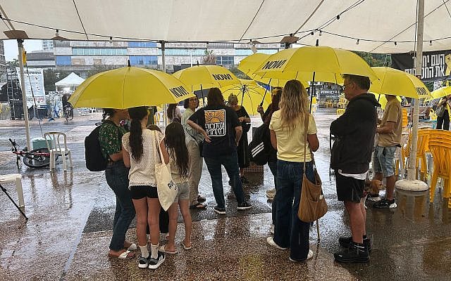 People shelter from the rain in Tel Aviv's Hostages Square on October 9, 2025. (Ben Sales/Times of Israel)
