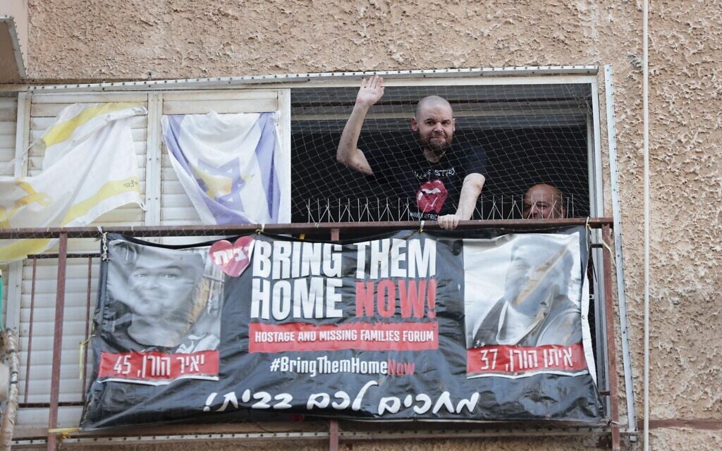 Released hostage Eitan Horn waves from the window of his home in Kfar Saba on October 16, 2025, as overjoyed neighbors throng the streets to welcome him.(Danor Aharon/Israeli Pro-Democracy Protest Movement)