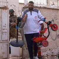 A paramedic helps a Palestinian family carry their belongings as an Israeli soldier enforces an evacuation order on a house in the Jenin refugee camp in the Israeli occupied West Bank on July 8, 2025. (Jaafar ASHTIYEH / AFP)