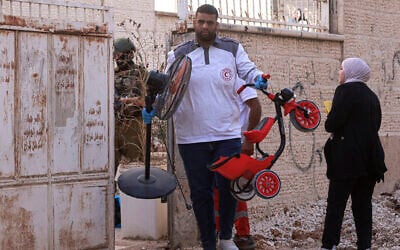 A paramedic helps a Palestinian family carry their belongings as an Israeli soldier enforces an evacuation order on a house in the Jenin refugee camp in the West Bank on July 8, 2025. (Jaafar ASHTIYEH / AFP)