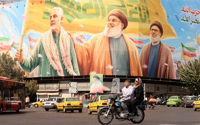 Iranians ride a motorcycle in front of a billboard depicting slain Lebanese Hezbollah leaders Hassan Nasrallah (C) and his successor Hashem Safieddine (R) as well as the late Iranian General Qasem Soleimani, in Tehran on September 28, 2025. (ATTA KENARE / AFP)