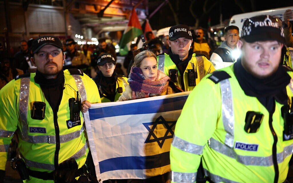 Police officers escort a woman with an Israeli flag near anti-Israel protesters outside Villa Park in Birmingham on November 6, 2025, ahead of the UEFA Europa League league-stage football match between Aston Villa and Maccabi Tel Aviv. (HENRY NICHOLLS / AFP)