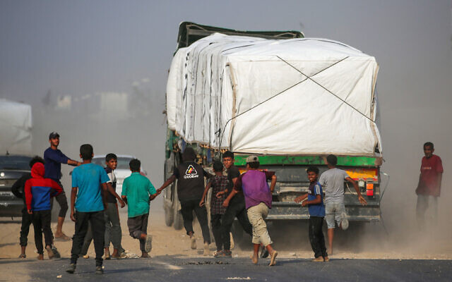 Illustrative: Displaced Palestinians chase after trucks traveling along Salah al-Din road in the central Gaza Strip, near Deir al-Balah, as they attempt to obtain humanitarian aid on November 9, 2025. (Eyad Baba/AFP)
