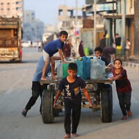 A boy pulls a donkey cart laden with containers carrying potable water, as other Palestinian children help push it along a road in the Bureij refugee camp in the central Gaza Strip on November 10, 2025. (Eyad Baba / AFP)