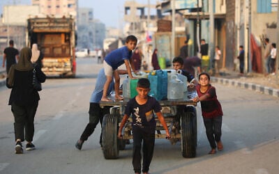 A boy pulls a donkey cart laden with containers carrying potable water, as other Palestinian children help push it along a road in the Bureij refugee camp in the central Gaza Strip on November 10, 2025. (Eyad Baba / AFP)