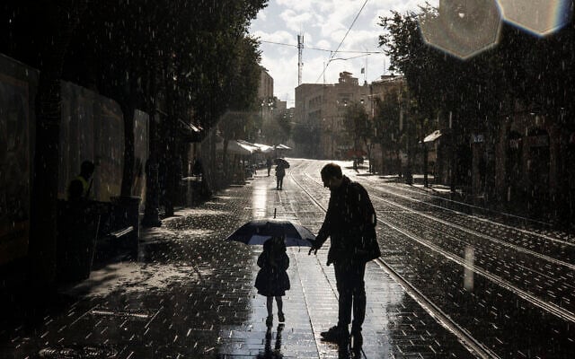 A young girl walks along a street with an umbrella as the first winter rain falls in Jerusalem on November 14, 2025. (John Wessels/AFP)
