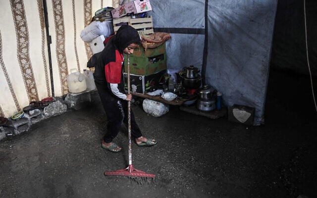 A Palestinian boy clears water from his shelter after the first winter rainfall in a displacement camp in Gaza City on November 14, 2025. (Omar al-Qattaa/AFP)