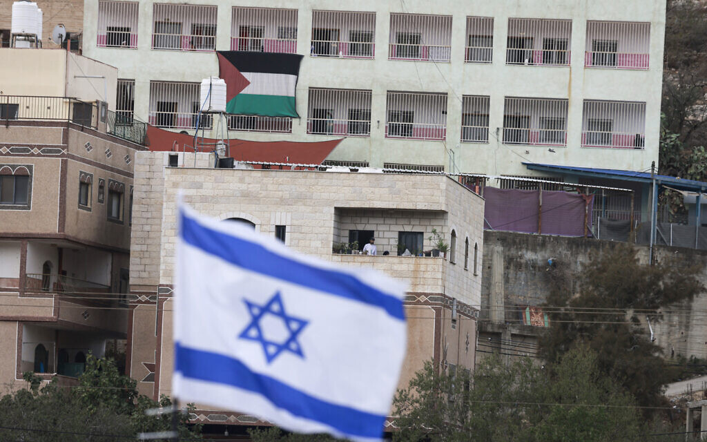 A Palestinian flag is seen on a building opposite an Israeli flag placed at the entrance of As-Sawiyah village, south of Nablus in the West Bank, on November 16, 2025. (Jaafar ASHTIYEH / AFP)