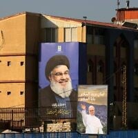 A poster of Pope Leo XIV hangs near a billboard of assassinated Hezbollah leader Hassan Nasrallah on the highway that leads to Beirut's international airport on November 20, 2025. (Photo by Anwar AMRO / AFP)