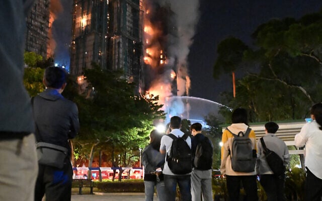26 Kasım 2025'te Hong Kong'un Tai Po bölgesindeki Wang Fuk Court konut sitesinde çıkan büyük yangın sırasında yükselen yoğun duman ve alevleri izleyenler. (Peter Parks/AFP)