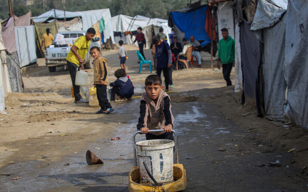 A boy pushes a bucket as children fill their containers with water at the Nuseirat camp for displaced Palestinians in the central Gaza Strip on November 29, 2025. (Eyad Baba / AFP) A boy pushes a bucket as children fill their containers with water at the Nuseirat camp for displaced Palestinians in the central Gaza Strip on November 29, 2025. (Eyad Baba / AFP)