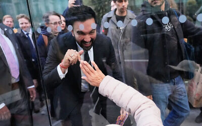 New York City mayoral candidate Zohran Mamdani waves to Rita Bellevue as she waits at a bus stop in New York, Oct. 27, 2025. (AP Photo/Seth Wenig)