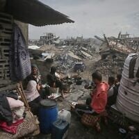 A family sits outside their damaged home, surrounded by the the rubble of neighboring residences, all devastated in the war in Gaza City, Nov.14, 2025. (AP Photo/Yousef Al Zanoun)