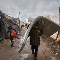 Salam Musa, 9, carries a mattress as he walks between tents after rainfall at a temporary camp in Deir al-Balah, in the central Gaza Strip, on Friday, November 14, 2025. (AP/Abdel Kareem Hana)