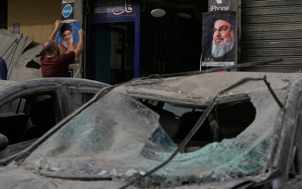 A man hangs a poster of Hezbollah's slain leader Hassan Nasrallah outside a shop as destroyed cars sit in the street following the Israeli airstrike that killed Hezbollah's chief of staff, Haytham Tabtabai, in the southern suburb of Hareit Hreik, Lebanon, Nov. 24, 2025. (AP Photo/Hassan Ammar)