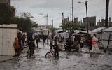 Palestinians walk through a flooded street next to a temporary tent camp after heavy rainfall in Deir al-Balah, central Gaza Strip, Tuesday, Nov. 25, 2025. (AP Photo/Abdel Kareem Hana)