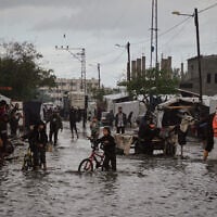 Palestinians walk through a flooded street next to a temporary tent camp after heavy rainfall in Deir al-Balah, central Gaza Strip, Tuesday, Nov. 25, 2025. (AP Photo/Abdel Kareem Hana)