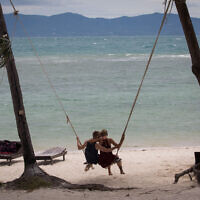 Illustrative: A couple sit on a swing hanging from the palm trees on a beach on Ko Pha Ngan island. August 15, 2017. Photo by (Nati Shohat/FLASH90)