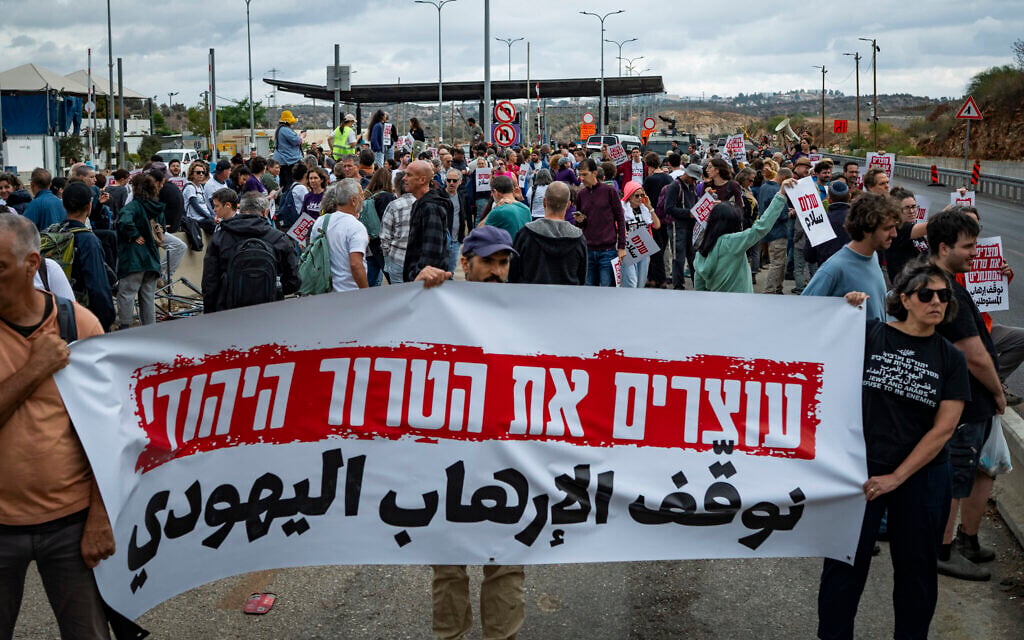 Activists from the Peace Now movement hold a sign reading, 'Stop Jewish terrorism,' at a checkpoint near the West Bank city of Ariel after police stopped buses that were on their way to a mass olive harvest in support of Palestinians facing attacks by extremist settlers, November 14, 2025. (Erik Marmor/Flash90)