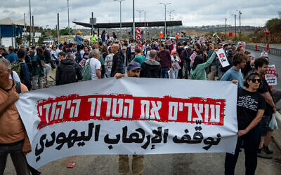 Activists from the Peace Now movement hold a sign reading, 'Stop Jewish terrorism,' at a checkpoint near the West Bank city of Ariel after police stopped buses that were on their way to a mass olive harvest in support of Palestinians facing attacks by extremist settlers, November 14, 2025. (Erik Marmor/Flash90)