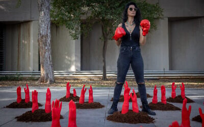 A woman wears punching gloves as mock red hands symbolizing slain women reach out of the ground in a protest display to mark the International Day for the Elimination of Violence against Women, outside Her Academy, a vocational school for survivors of prostitution and abuse, in Tel Aviv. November 24, 2025. (Miriam Alster/Flash90)