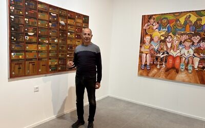 Curator Avi Ifergan from the Bar-David Museum in Kibbutz Bar'am on October 30, 2025, in front of two paintings by Noam Edry from her exhibit 'Red Day,' (Jessica Steinberg/Times of Israel)