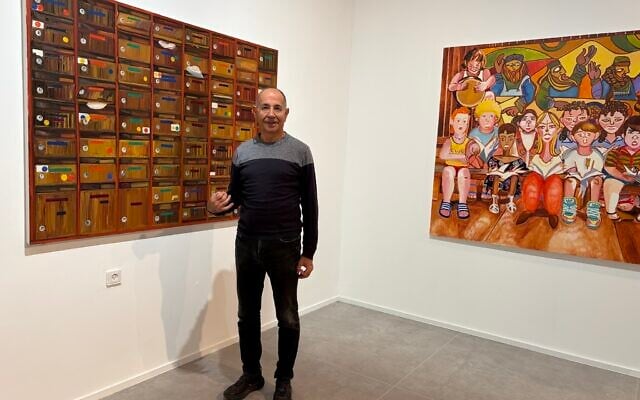 Curator Avi Ifergan from the Bar-David Museum in Kibbutz Bar'am on October 30, 2025, in front of two paintings by Noam Edry from her exhibit 'Red Day,' (Jessica Steinberg/Times of Israel)