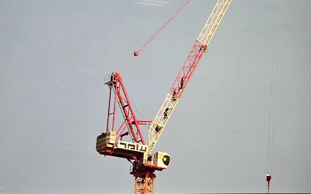 A teenage boy is seen on a platform hanging from the rope of a crane above a high-rise building as firefighters attempt to rescue him in Jerusalem on November 24, 2025.(Fire and Rescue Service)