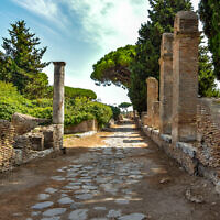 Ancient roman road and ruins with trees and cloudy sky in Ostia Antica. (Janos Varga/iStock by Getty Images)