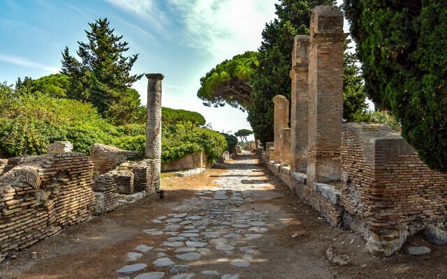 Ancient roman road and ruins with trees and cloudy sky in Ostia Antica. (Janos Varga/iStock by Getty Images)