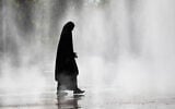 A woman wearing a hijab walks through the water spray in front of the Praterstern train station in Vienna on August 21, 2023. (Alex HALADA / AFP)