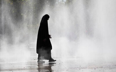 A woman wearing a hijab walks through the water spray in front of the Praterstern train station in Vienna on August 21, 2023. (Alex HALADA / AFP) A woman wearing a hijab walks through the water spray in front of the Praterstern train station in Vienna on August 21, 2023. (Alex HALADA / AFP)