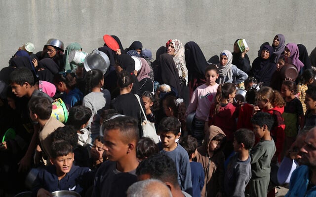 Displaced Palestinians, children and adults wait for food at a shelter in Nuseirat, in the central Gaza Strip, on November 23, 2025. (EYAD BABA / AFP) Displaced Palestinians, children and adults wait for food at a shelter in Nuseirat, in the central Gaza Strip, on November 23, 2025. (EYAD BABA / AFP)