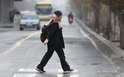 An Iranian woman walks across a crosswalk as the first winter rains soak the Iranian capital following one of the driest years in Tehran, December 2025. (ATTA KENARE / AFP)