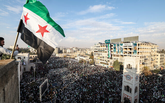 A Syrian flag flutters above crowds gathering during celebrations marking one year since the overthrow of the Assad regime, in central Hama, Syria, on December 5, 2025. (OMAR HAJ KADOUR / AFP) A Syrian flag flutters above crowds gathering during celebrations marking one year since the overthrow of the Assad regime, in central Hama, Syria, on December 5, 2025. (OMAR HAJ KADOUR / AFP)